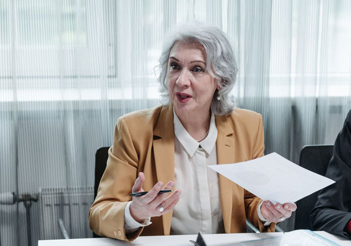 An older woman with grey hair explaining financial documents resembling a MIL. An older woman with grey hair explaining financial documents resembling a MIL.