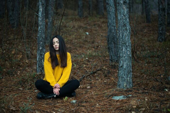 A woman sitting cross-legged in a forest with eyes closed, reflecting on realizing her friends were haters.