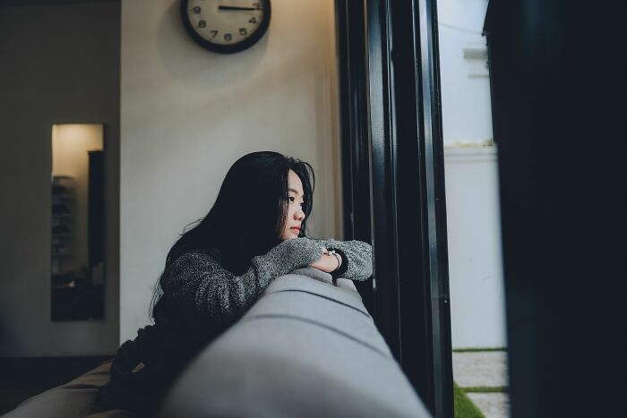 A pensive woman stares out a window, contemplating if friends are actually haters.
