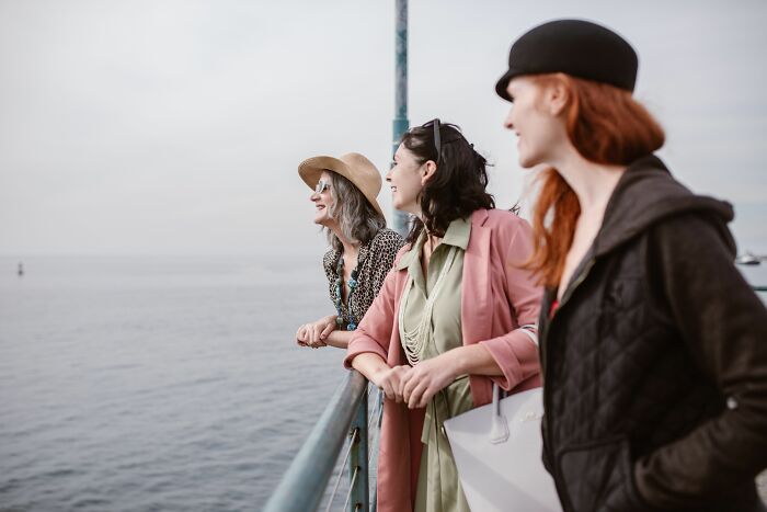 Three friends laugh by the ocean, unaware that one may realize a friend is a hater.
