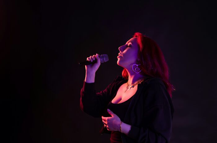 Singer with red hair on stage, microphone in hand, secrets coming to light after people keeping them were gone.