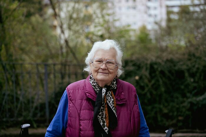 Smiling elderly woman outdoors, wearing glasses and a vest, secrets revealed after people keeping them were gone.