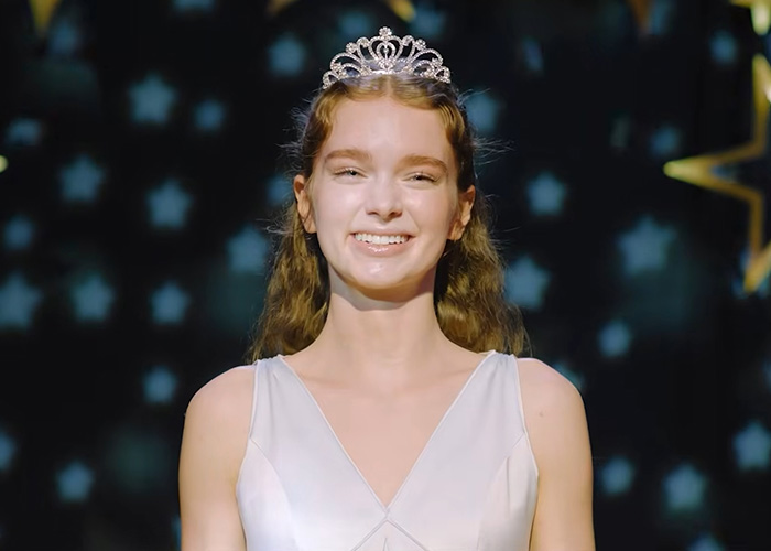 A young woman in a white dress and tiara smiles, with a star-patterned background, from a Gen Z Stephen King adaptation. A young woman in a white dress and tiara smiles, with a star-patterned background, from a Gen Z Stephen King adaptation.