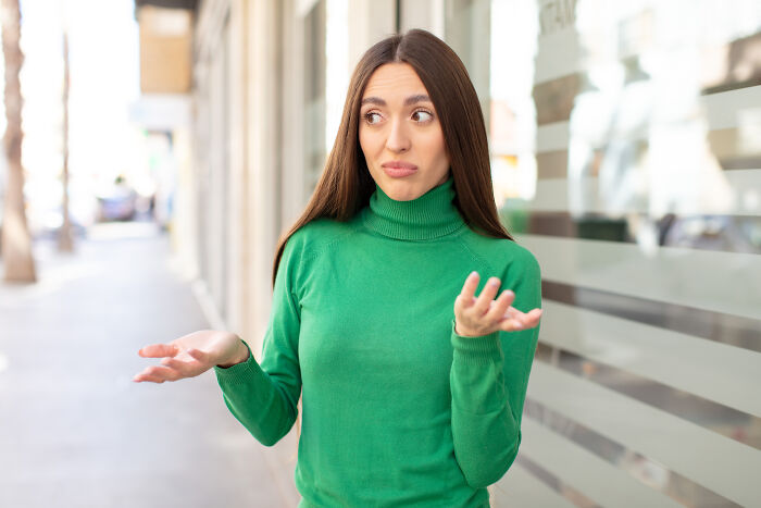 A woman in a green sweater shrugs in confusion, illustrating a reaction to subtle sexism.
