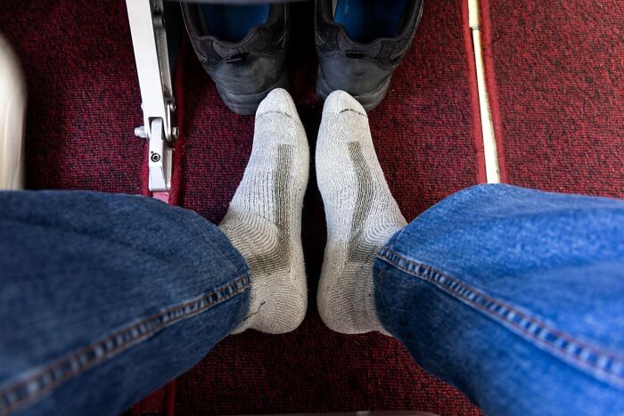 A close-up of a person's feet in socks on an airplane floor, highlighting a common plane seatmate annoyance.