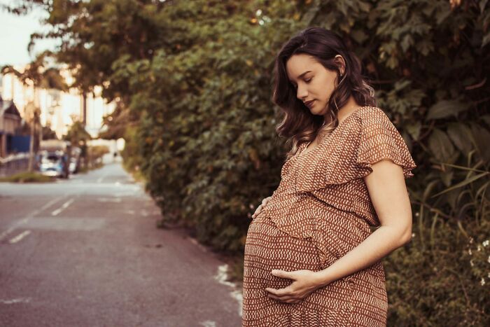 A pregnant woman in a patterned dress holding her belly outdoors, reflecting maternal health medical practices