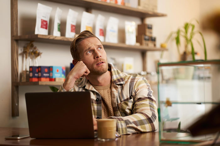 Man looking thoughtfully beside laptop in cafe, reflecting on martial arts relationship issues Man looking thoughtfully beside laptop in cafe, reflecting on martial arts relationship issues