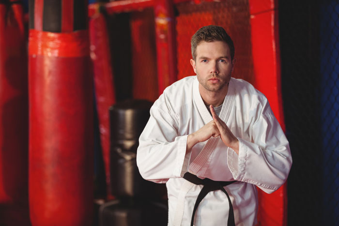 Man in martial arts uniform posing in gym with red punching bags in background Man in martial arts uniform posing in gym with red punching bags in background