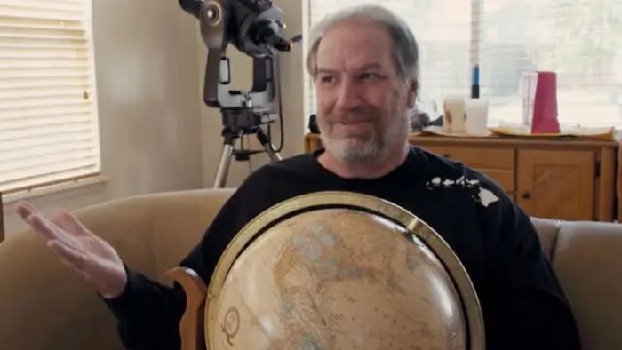 A man with a beard holds a globe, questioning the flat Earth theory. A man with a beard holds a globe, questioning the flat Earth theory.