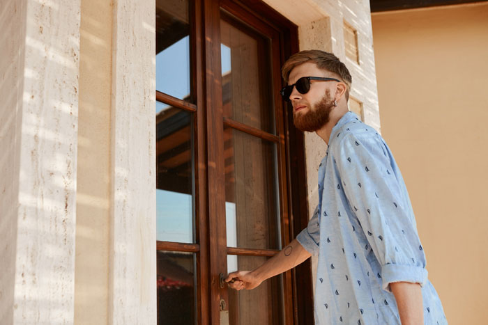 A man with a beard and sunglasses, wearing a blue shirt, opening a door to leave after a breakup. A man with a beard and sunglasses, wearing a blue shirt, opening a door to leave after a breakup.