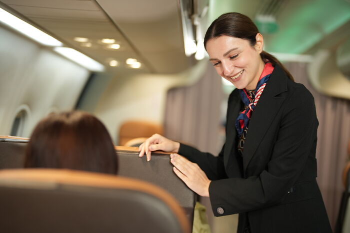 A smiling flight attendant interacting with a passenger onboard, showing things a passenger could do.