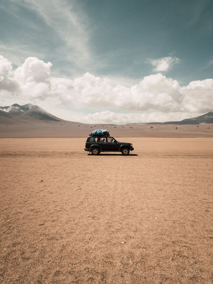 An SUV driving across a vast, barren desert landscape under a wide sky, reflecting US stereotypes.