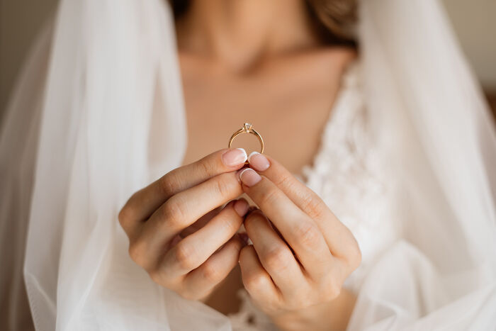A bride holds her wedding ring, contemplating her life choices and marriage regrets