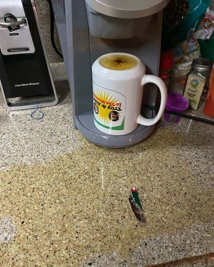 A coffee maker pours coffee onto an upside-down mug on a kitchen counter, a serious kitchen fail.