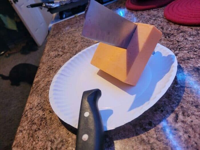 A knife stuck through a block of cheese on a paper plate, showcasing kitchen fails.