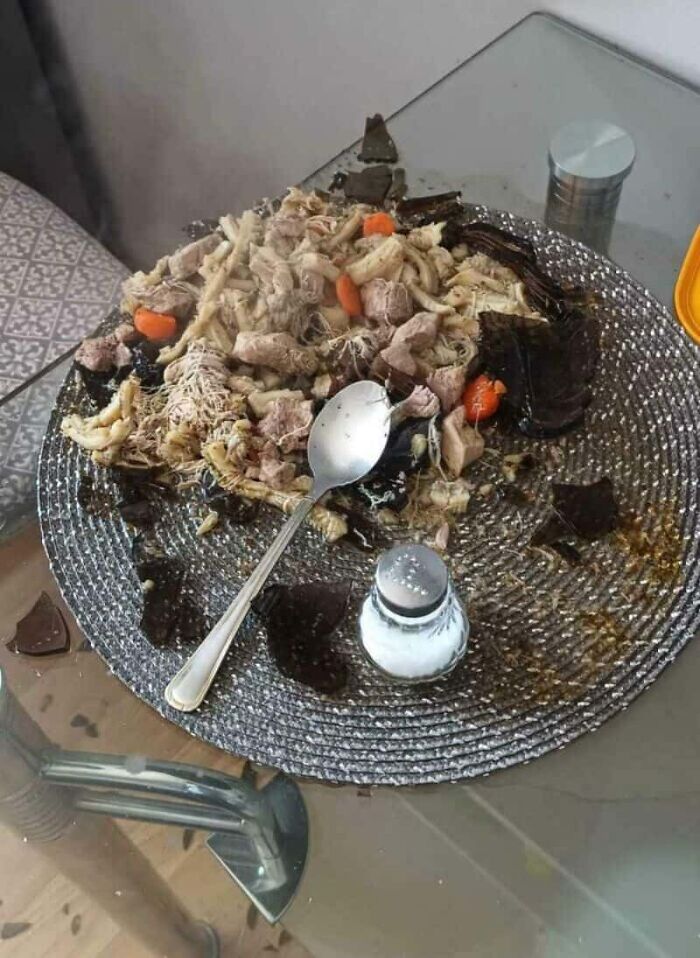 A broken glass plate with food and glass shards on a table, a disastrous kitchen fail.