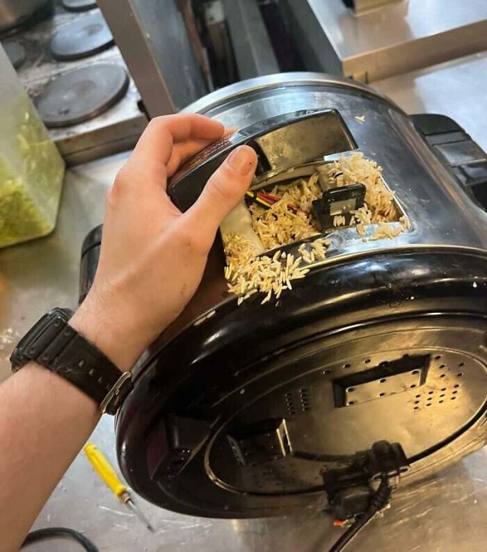 A hand holding a broken rice cooker filled with rice, showcasing unfortunate kitchen fails.