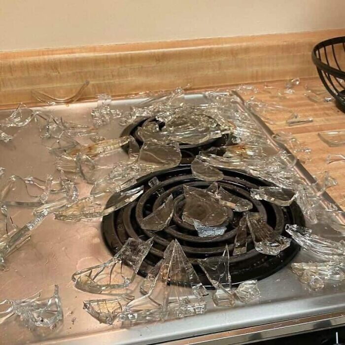 Shards of glass from a broken pot cover scattered across a stovetop, an unfortunate kitchen fail.