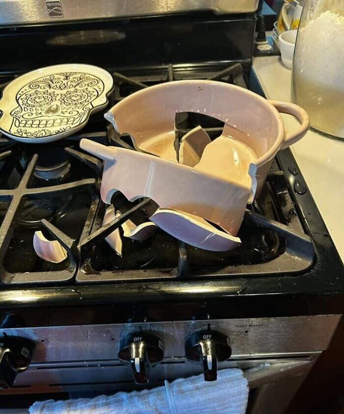 Shattered pink ceramic pot on a black gas stovetop next to a decorative skull plate, a dramatic kitchen fail.