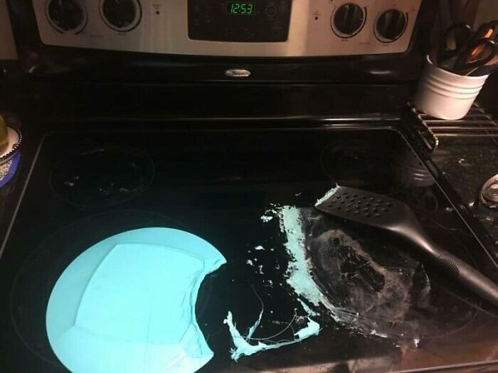Smashed light blue plate and spilled food on a black electric stovetop, illustrating a messy kitchen fail.