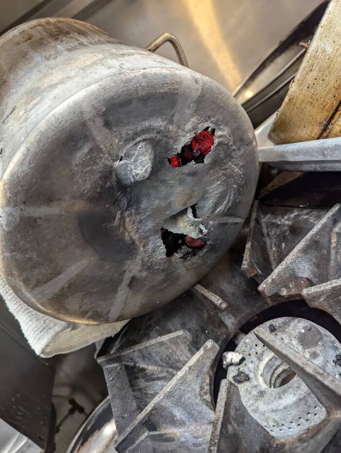 Close-up of a melted aluminum pot with holes, a kitchen fail showing fire damage on a stovetop.