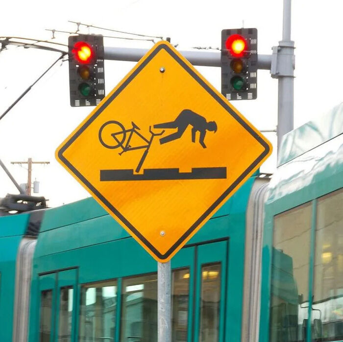 A yellow warning sign depicting a bicyclist crashing onto light rail tracks, showing signs around the world.