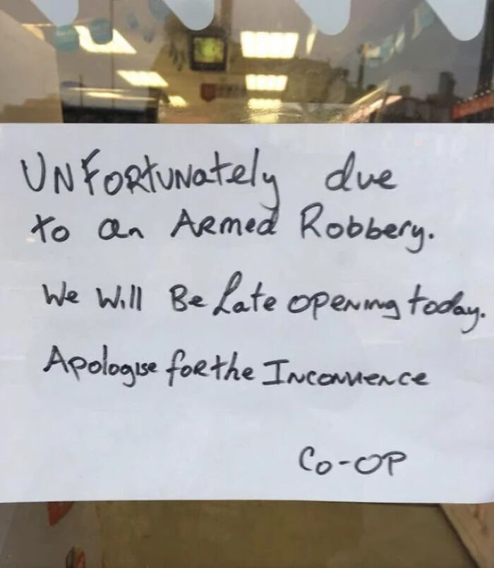 Handwritten sign on a door apologizing for late opening due to an armed robbery, showing signs from around the world.