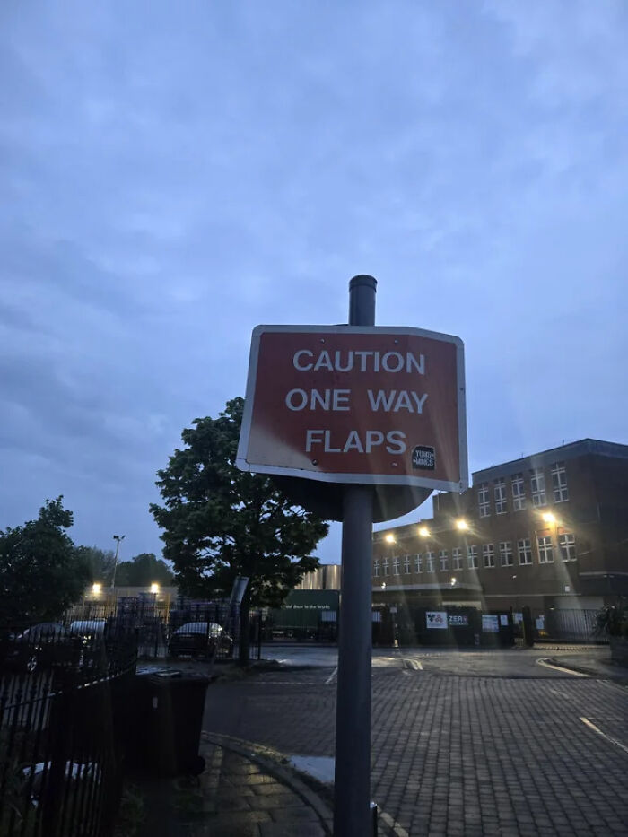 An street sign reading Caution One Way Flaps in an industrial area, highlighting funny signs from around the world.