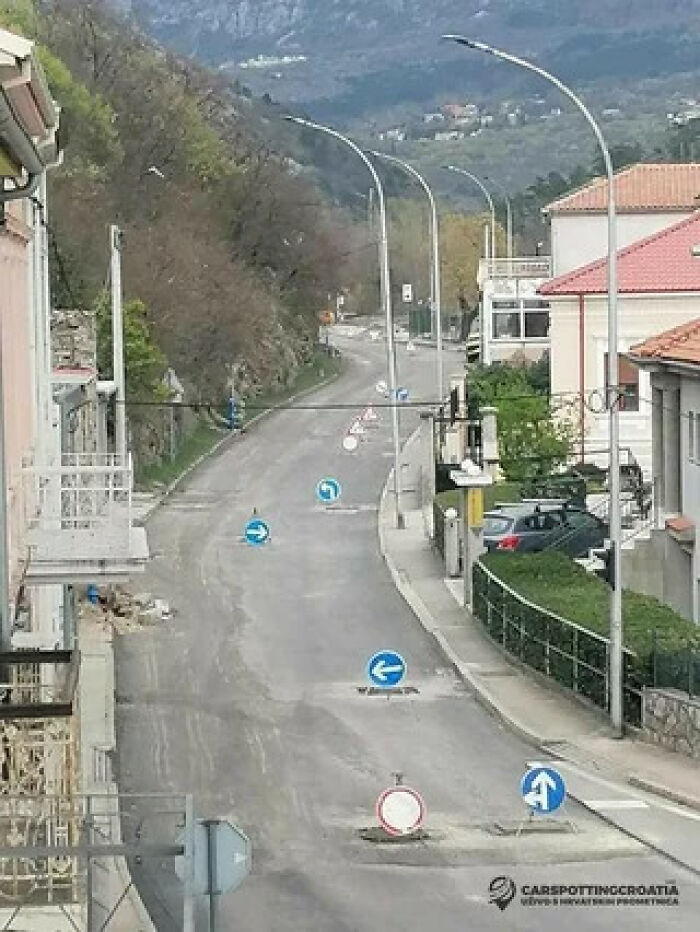 An overhead view of a street cluttered with multiple conflicting blue arrow signs on the road surface.
