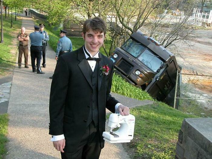 A man in a tuxedo holding a sewing machine next to an unhinged UPS truck accident.