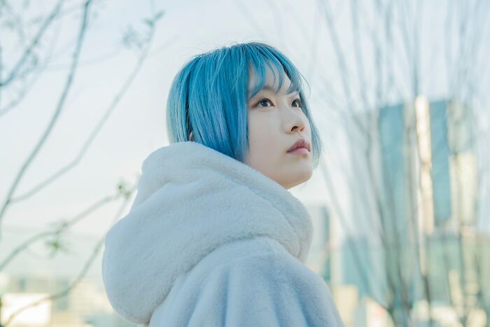 Young person with blue hair looking up thoughtfully, considering going no contact with a parent.