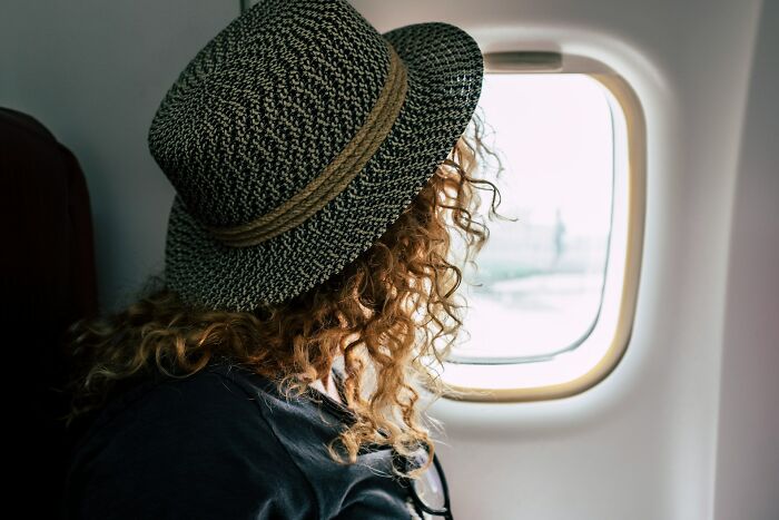 A female passenger wearing a hat and looking out of a plane window