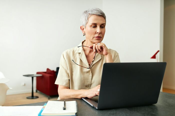 A woman with short grey hair working on her laptop, contemplating going no contact with a parent.