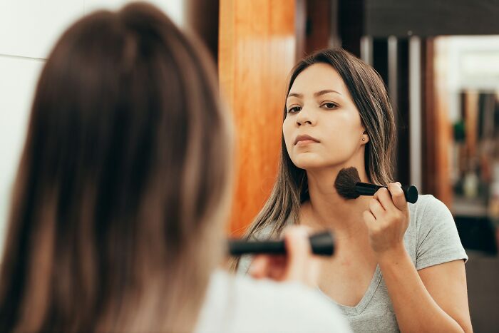 A woman applying makeup in the mirror, noticing subtle body changes in her 30s and 40s.