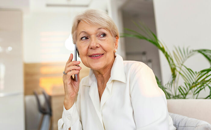 A senior woman smiling and talking on her phone, as if she overheard something she wasnt meant to hear.