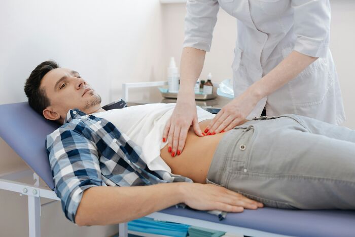 A doctor examines a man's abdomen on an examination table due to extreme illness and sickness.