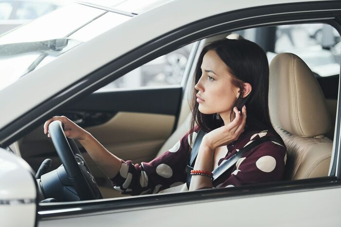 A woman inside a car, looking away, reflecting things people do that others judge them for.