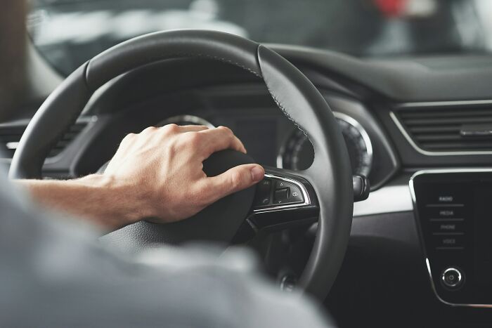 A persons hand pressing a car horn, highlighting a common US stereotype about driving.