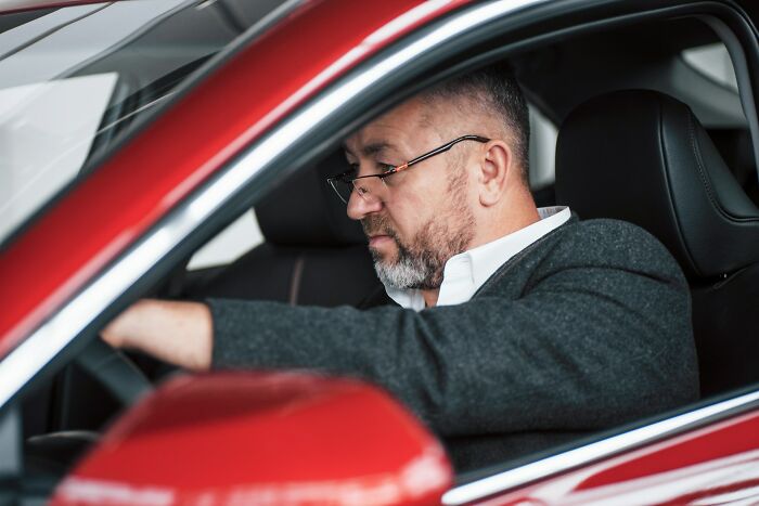 A man in a red car, looking serious, representing a client perhaps contemplating legal advice or past actions.