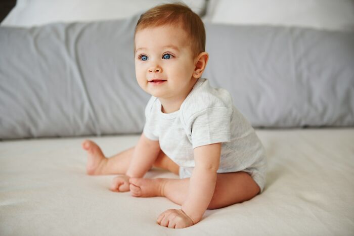 A happy baby sitting on a bed, representing historical pediatric medical practices