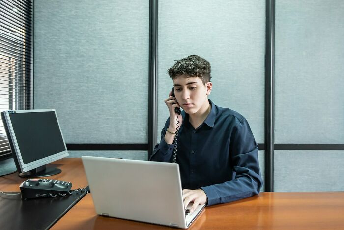 A young man in a blue shirt on the phone, looking at a laptop, illustrating stupid things people said.