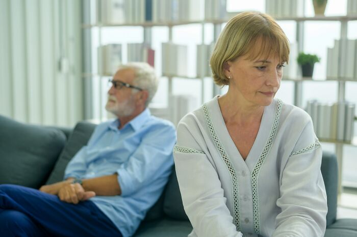 Distressed middle-aged couple sitting separately on a couch, potentially from going no contact with a parent.