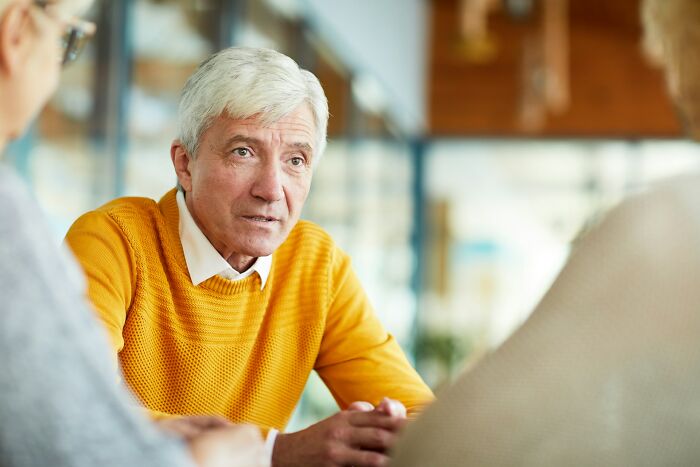 A man with gray hair in a yellow sweater looks intently at someone off-camera, considering going no contact with a parent.