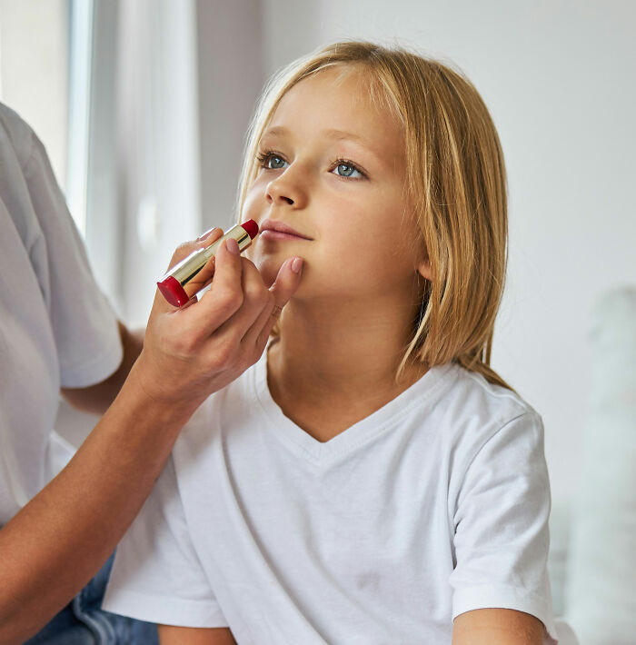 A young girl having lipstick applied, potentially overhearing something she wasn't meant to hear.