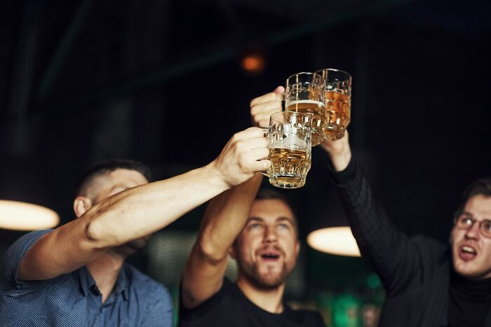 Three men toasting with beer mugs, celebrating, with one man looking up towards the glasses.