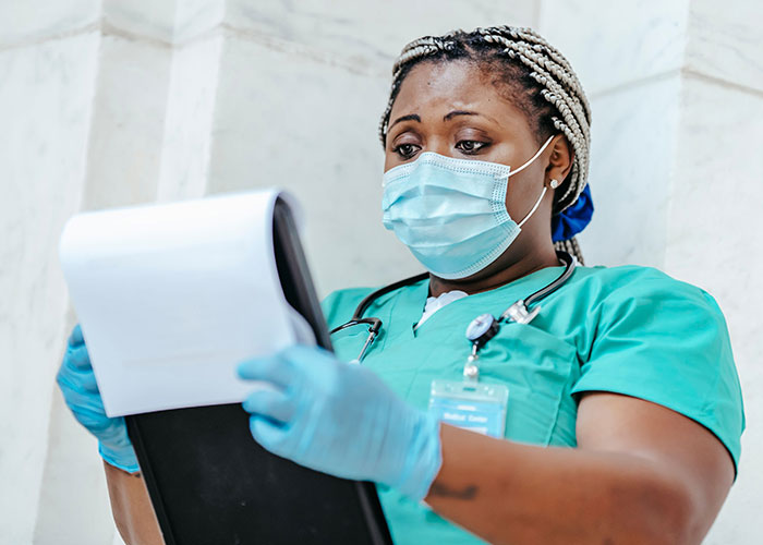 A nurse wearing a mask and gloves looks closely at a medical clipboard. A nurse wearing a mask and gloves looks closely at a medical clipboard.