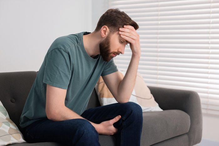 A stressed man sits on a couch holding his head, overwhelmed by family drama. A stressed man sits on a couch holding his head, overwhelmed by family drama.
