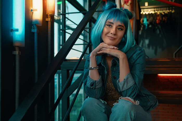 Woman with blue hair sitting indoors with relaxed expression