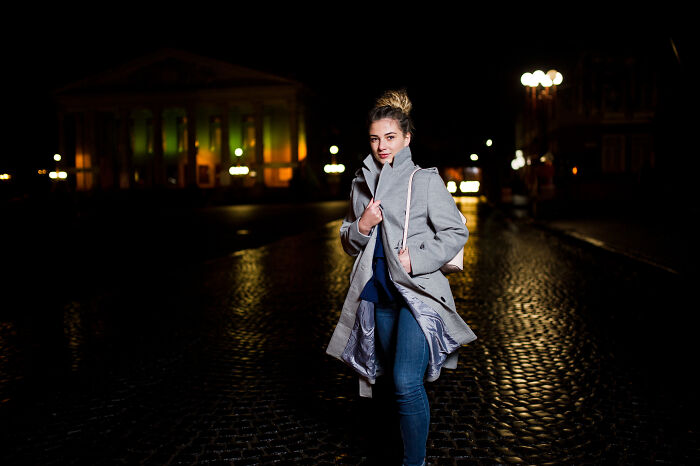 A woman walking alone on a dark wet street at night, highlighting safety concerns and subtle sexism