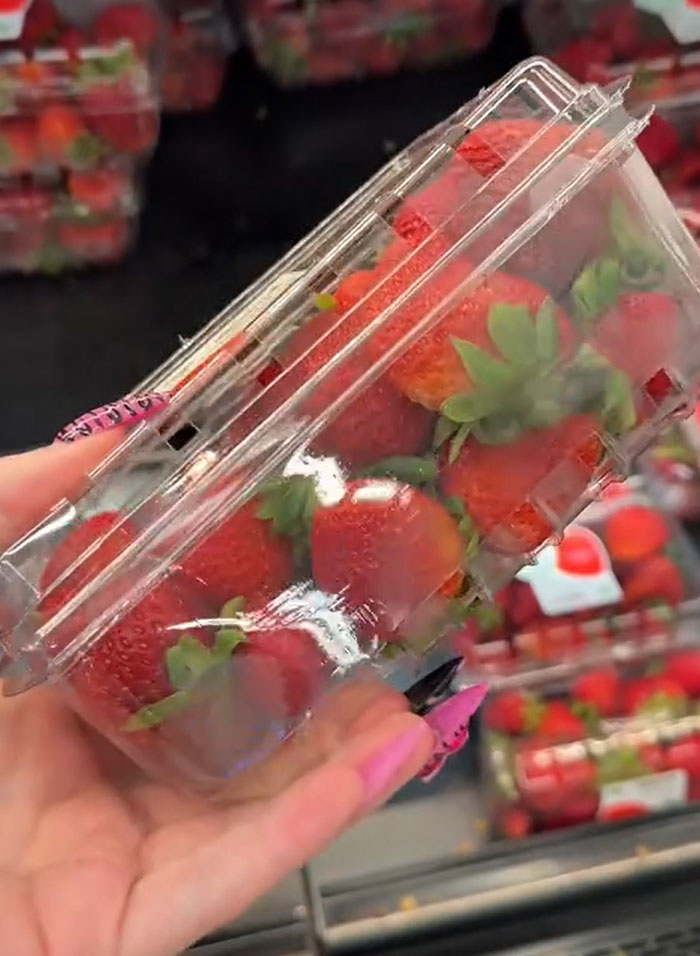 Hand holding a plastic container of fresh red strawberries, a common item in American parents' grocery carts. Hand holding a plastic container of fresh red strawberries, a common item in American parents' grocery carts.
